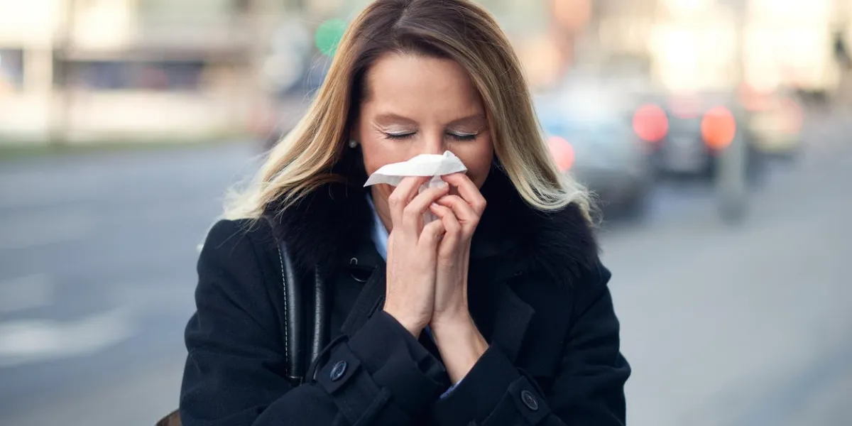 woman with a seasonal winter cold blowing her nose on a handkerchief or tissue as she walks down an urban street in a health and medical concept