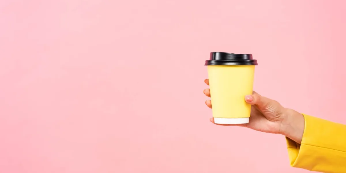 cropped view of woman holding yellow disposable cup of coffee, isolated on pink