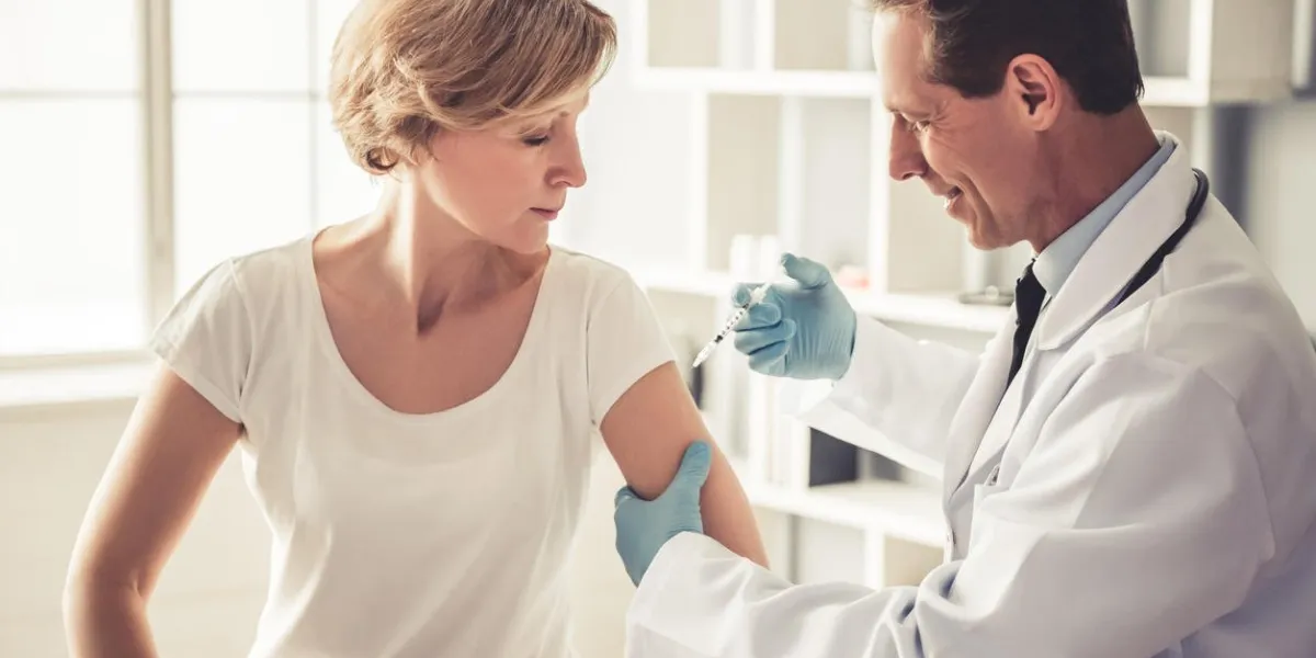 handsome mature doctor in white coat is making woman an injection and smiling while working in office