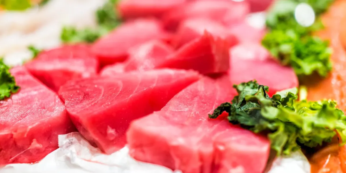 seafood stand with cuts of red pink farmed wild tuna steaks on ice with kale leaves