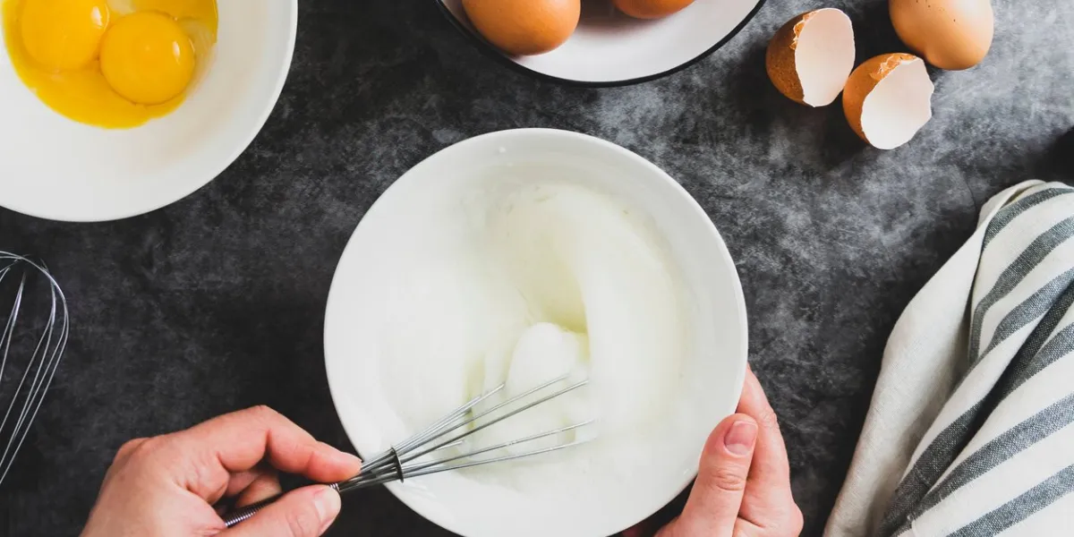 whipping white eggs with whisk, in a palte top view of woman's hands mixing eggs, cooking pastry