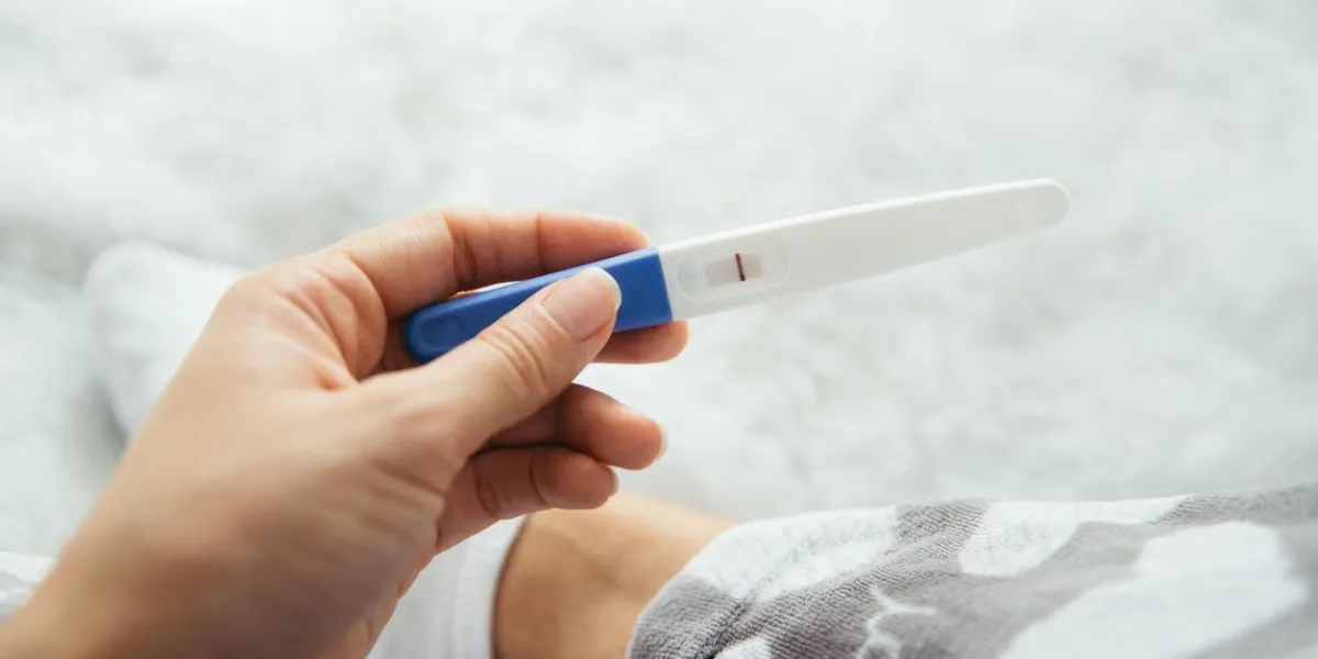upset woman lie sad in white bed with negative pregnancy test