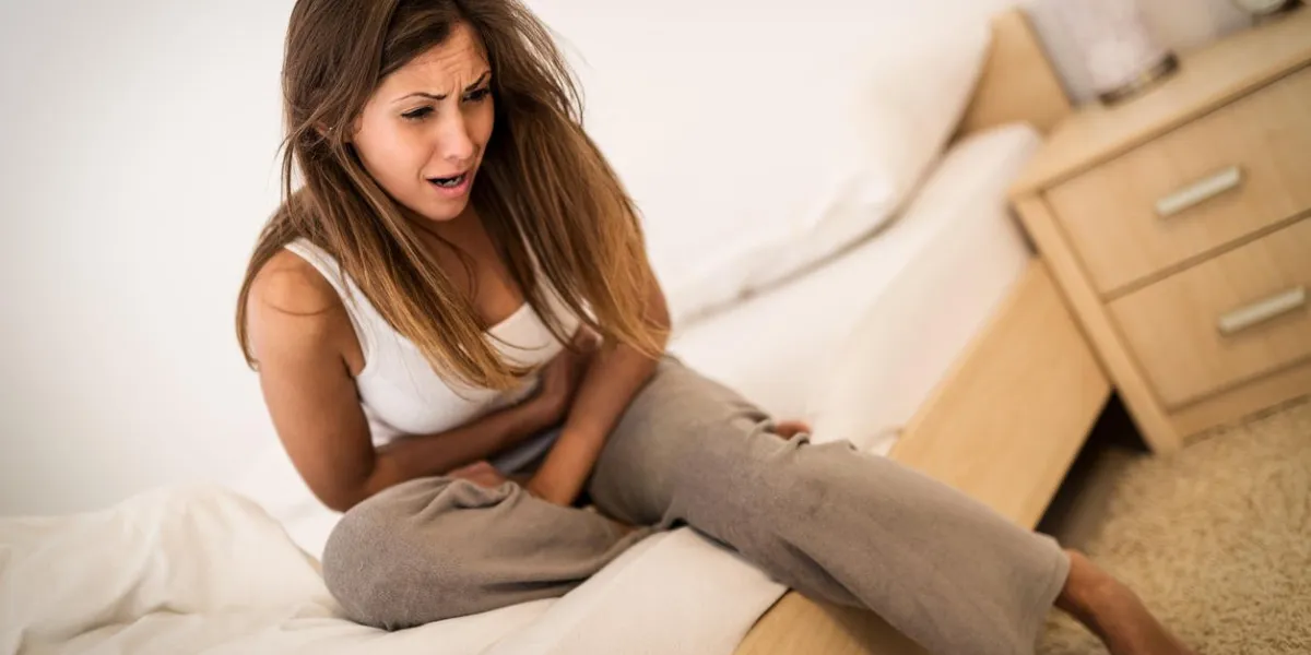beautiful young woman sitting on bed and holding hands on her stomach