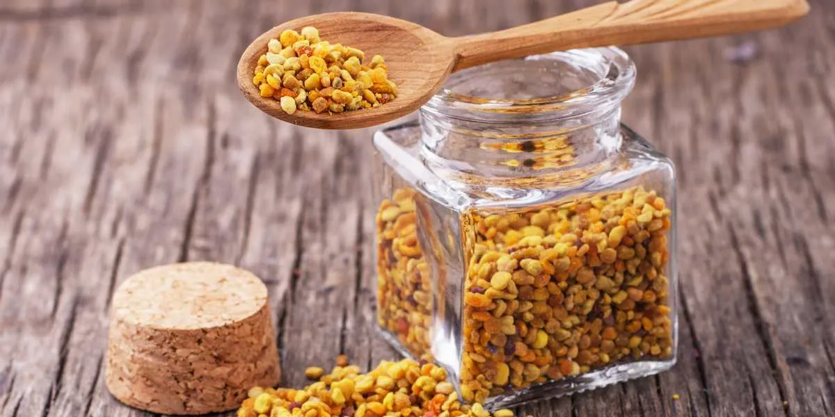 golden bee pollen in small glass jars with honey comb on the texture wooden background with the wooden spoon concept of healthy food selective focus