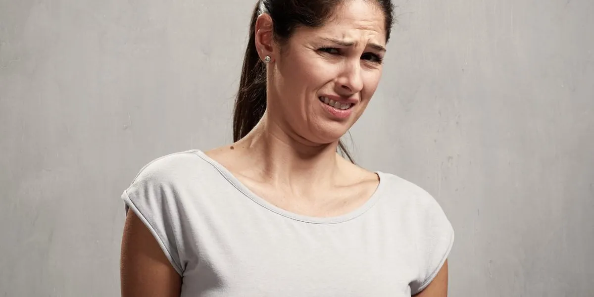 young woman disgusted squeamishness over gray wall background