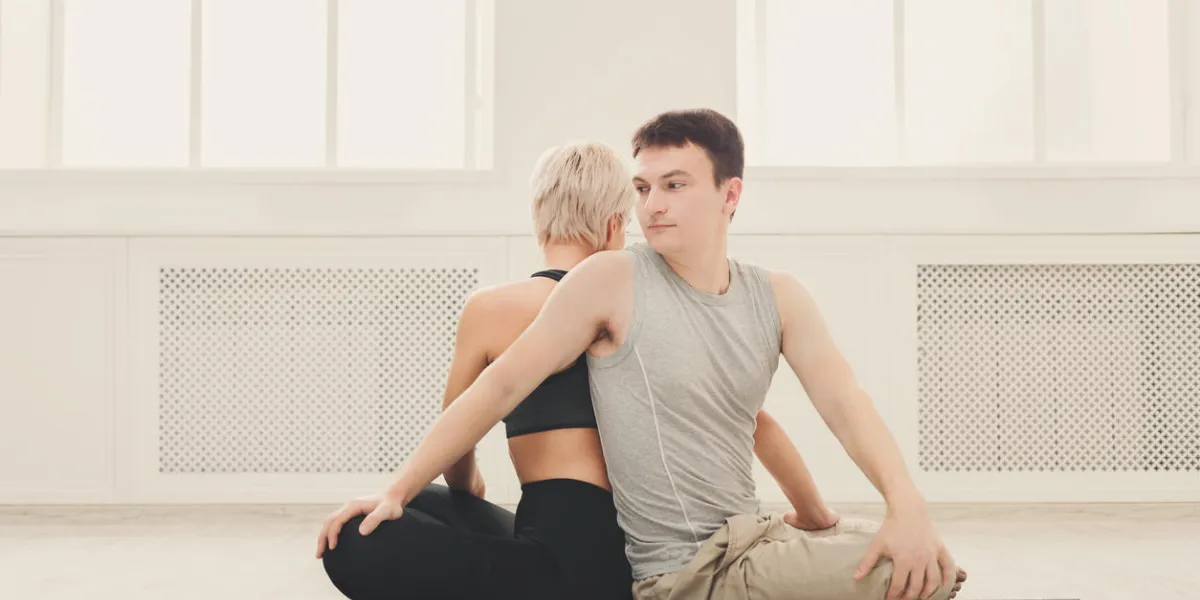 young couple practicing yoga together man and woman sitting near back to back on mat and twisting around partner, copy space