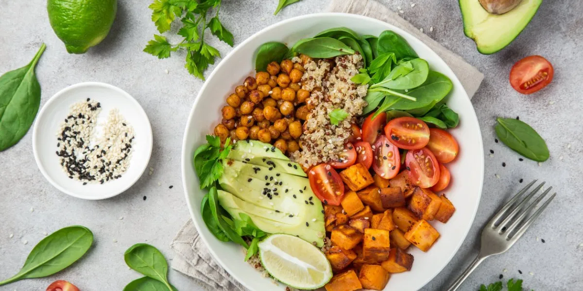 healhty vegan lunch bowl with ingredients avocado, quinoa, sweet potato, tomato, spinach and chickpeas vegetables salad top view