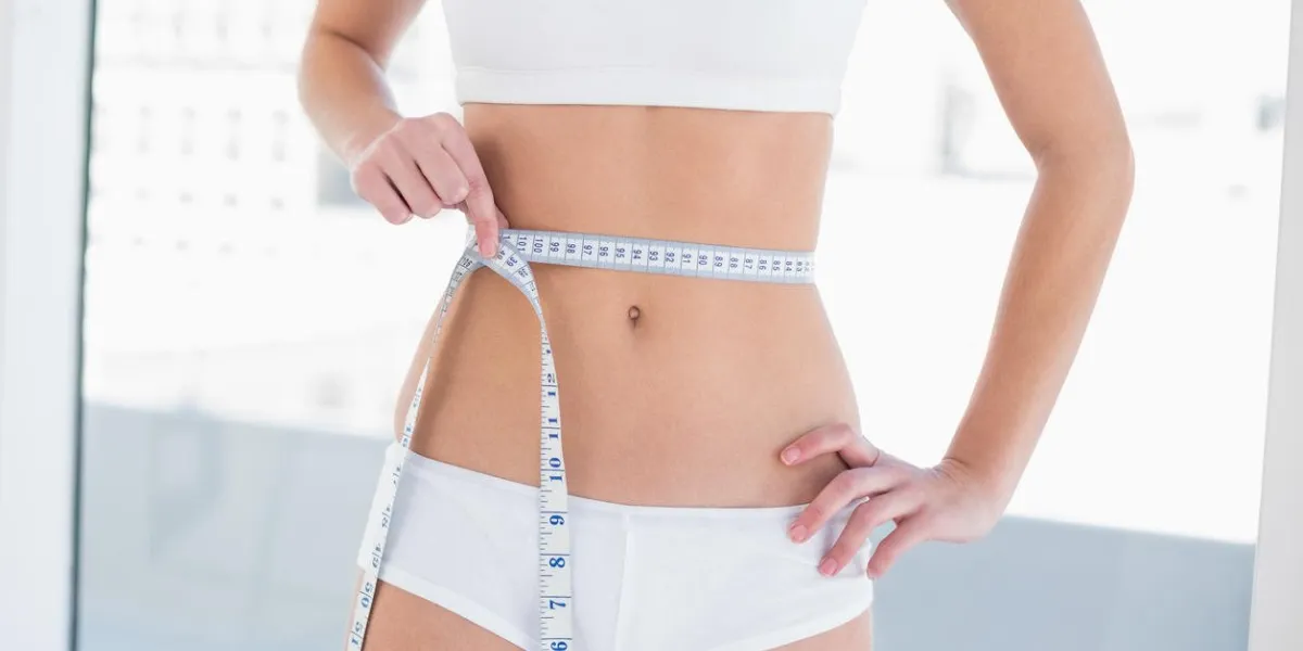 close up of a slim woman in white sportswear measuring her waist