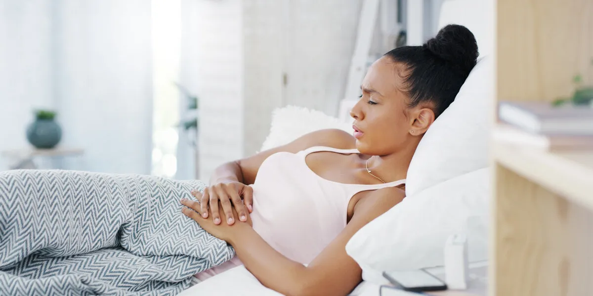 woman in bed, stomach pain and menstruation cramps with endometriosis, health problem and sick female person with digestion issue, abdominal ache and period with gastrointestinal emergency at home