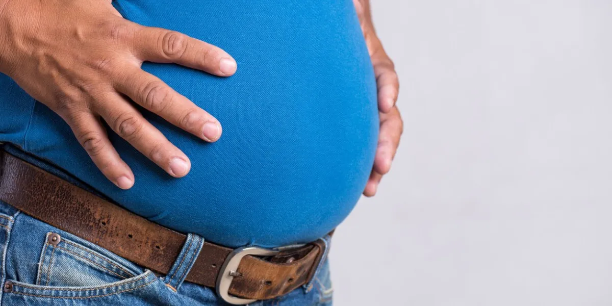 overweight or fat adult man in very tight jeans on a gray background healthcare, medicine concept