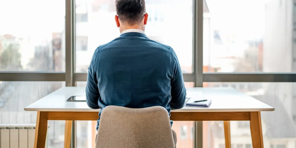 rear view of businessman working at desk while sitting in front of windows at corporate office