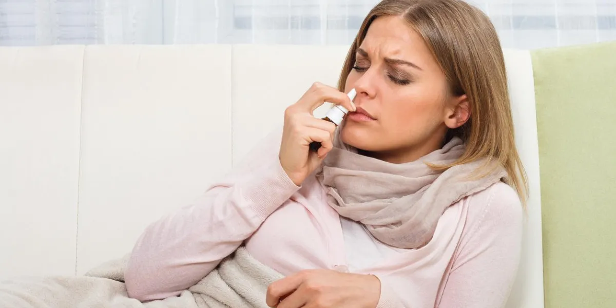 femme a la grippe et elle utilise un spray nasal pour s'aider