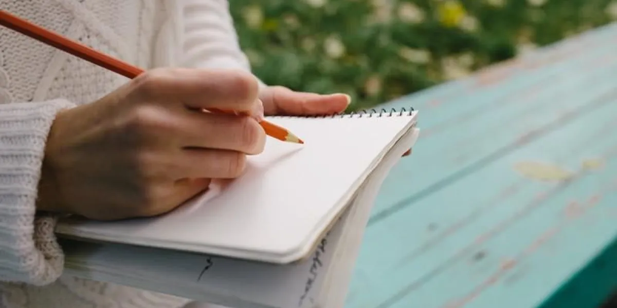 femme dessine un crayon de couleur dans un cahier extérieur fermer de pavé ouvert dans les mains féminines avec un stylo assis sur les escaliers dans le parc