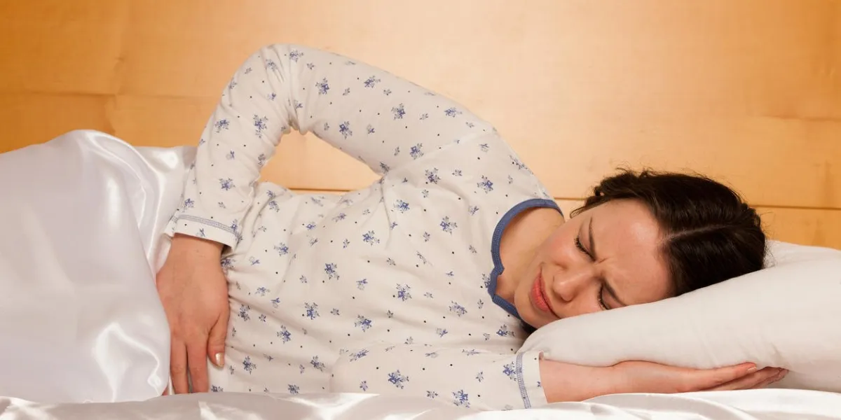 asian caucasian woman with pain in her stomcah lying in bed and holding belly