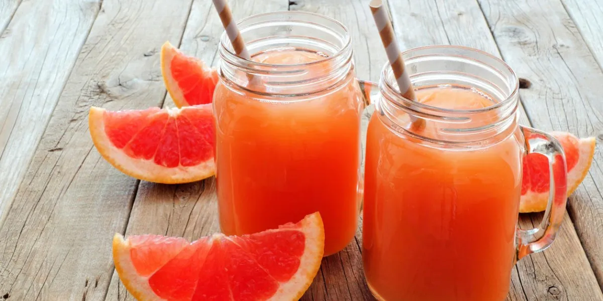 deux verres de pot mason de jus de pamplemousse avec des tranches et des pailles sur fond en bois rustique