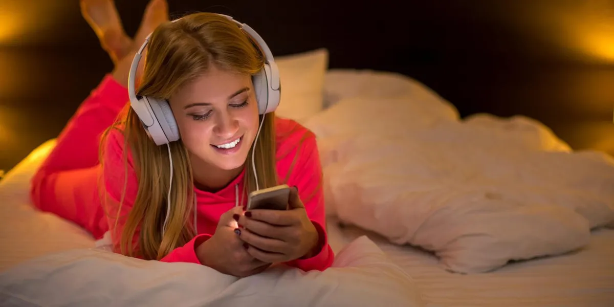 jeunes jolies femmes blondes souriantes en écoutant de la musique avec un casque d'un smartphone allongé sur le lit à la maison