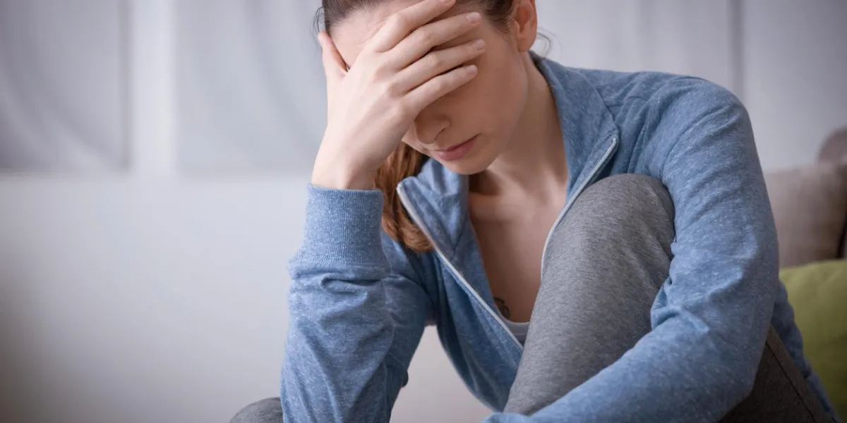 sad depressed woman at home sitting on the couch, looking down and touching her forehead, loneliness and pain concept