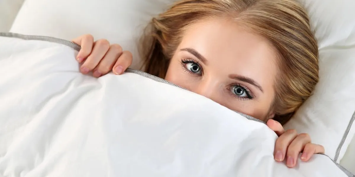 belle femme blonde se cachant le visage sous la couverture couché dans le lit yeux féminins étincelants à la recherche dans la caméra gros plan rêves, flirt, jeu, se réveille dans le lieu étrange, la honte, le concept de sexe décontracté
