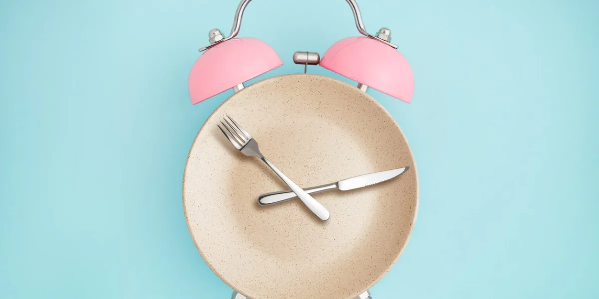 alarm clock and plate with cutlery concept of intermittent fasting, lunchtime, diet and weight loss