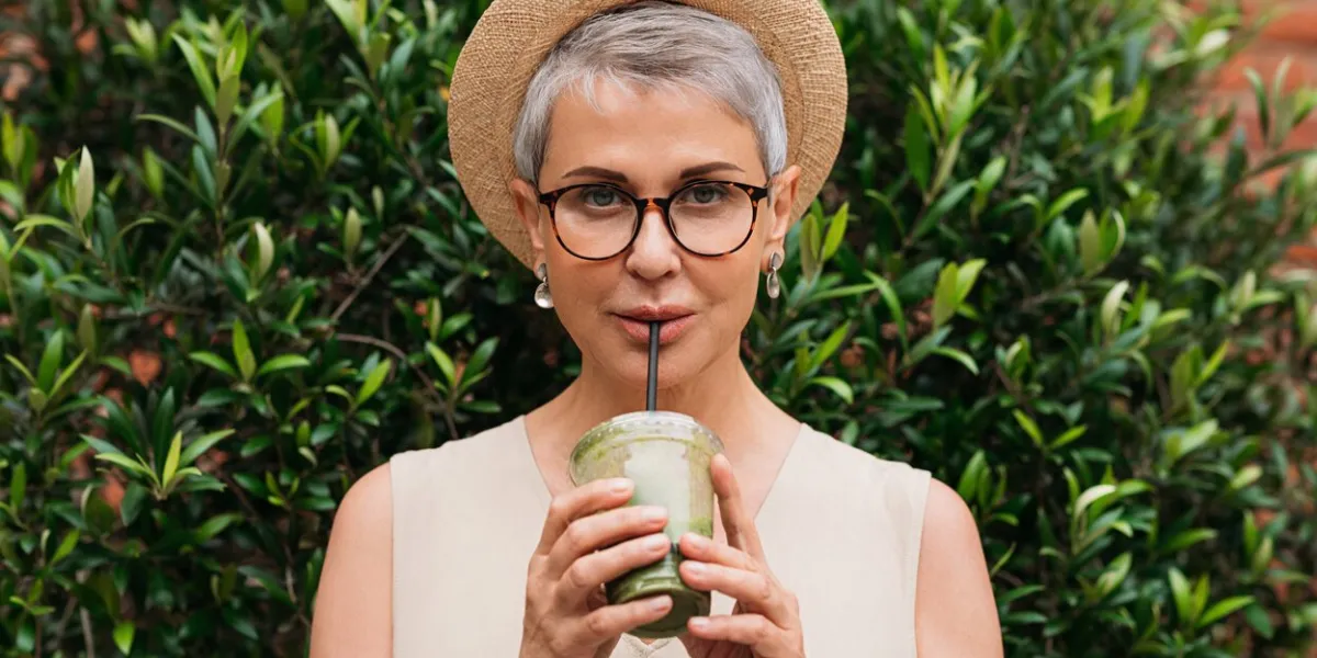 stylish mature woman with grey hair drinking matcha latte outdoors