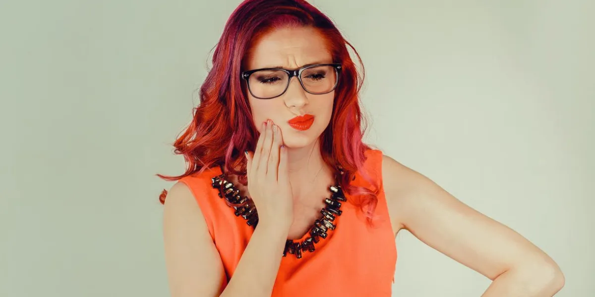 dental care, toothache closeup portrait of young woman with sensitive tooth ache about to cry from pain touching outside mouth with hand, isolated green background negative emotion facial expression