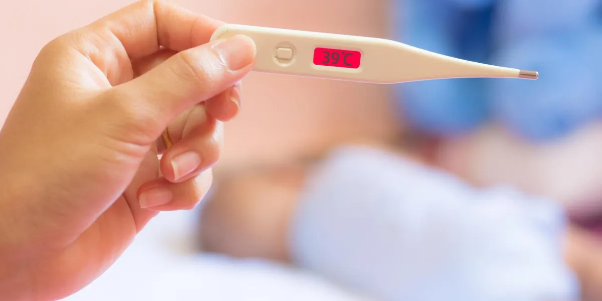 thirty-nine degrees on medical thermometer in mother hand, and infant asleep on white mattress measuring fever in babies concept