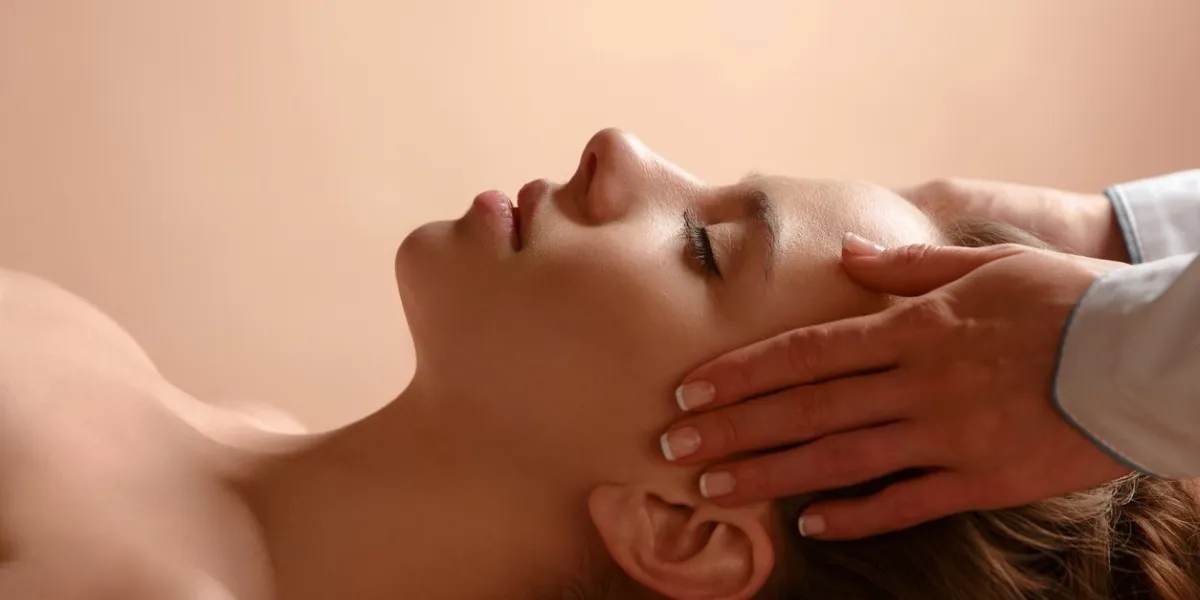 the masseuse makes relaxing head massage and spa client to young girl close-up of face and hands brown light warm background