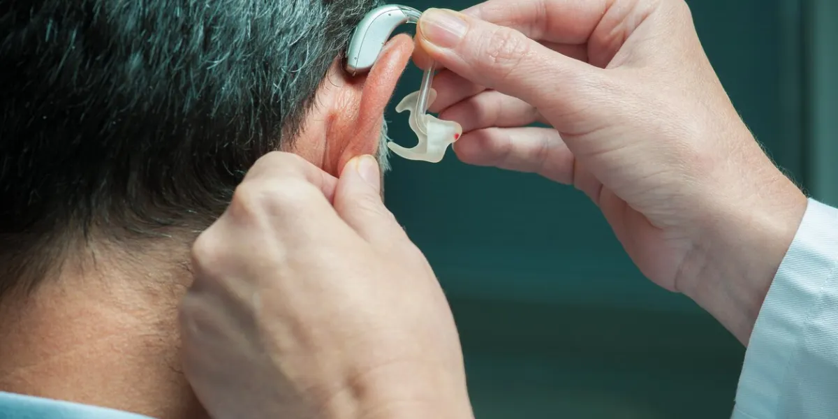 doctor inserting hearing aid in man's ear