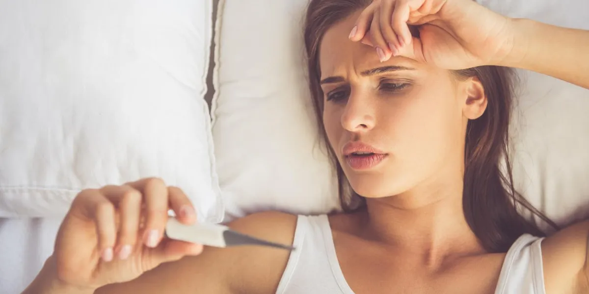 top view of beautiful sick young woman looking at thermometer while lying in bed at home