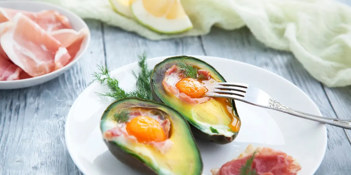 two baked avocado halves with egg on a white saucer healthy breakfast for the keto diet
