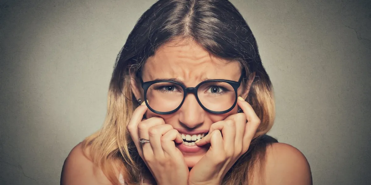 closeup portrait nervous stressed young woman girl in glasses student biting fingernails looking anxiously craving something isolated on grey wall background human emotion face expression feeling