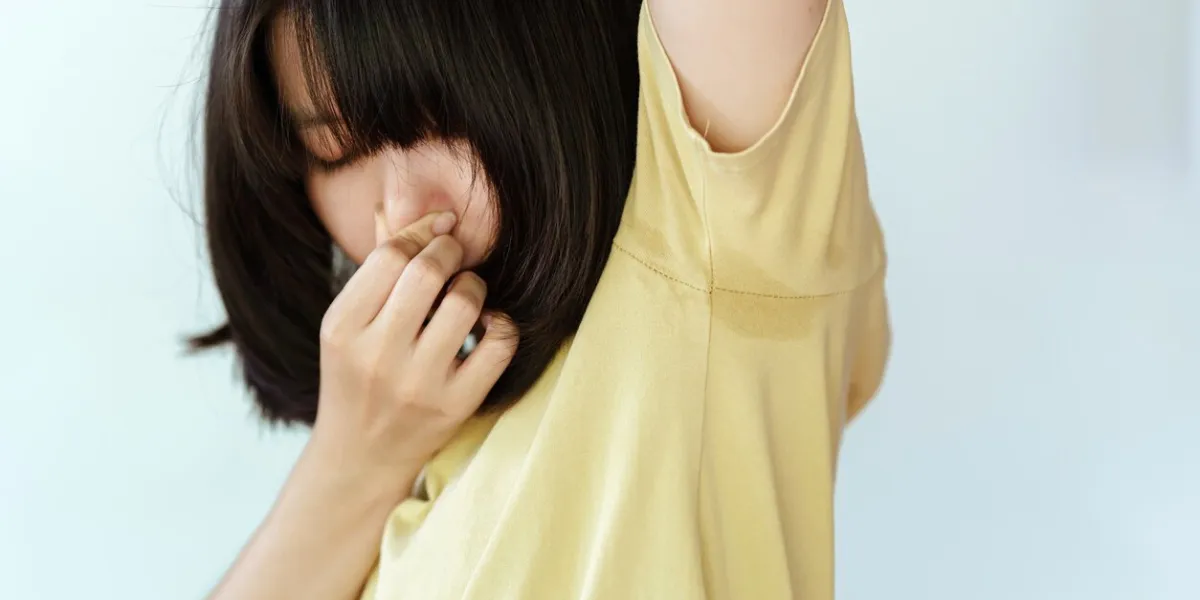 the woman in the yellow shirt covered her nose with her hands because she was sweating in her armpits and had a bad smell health care concept
