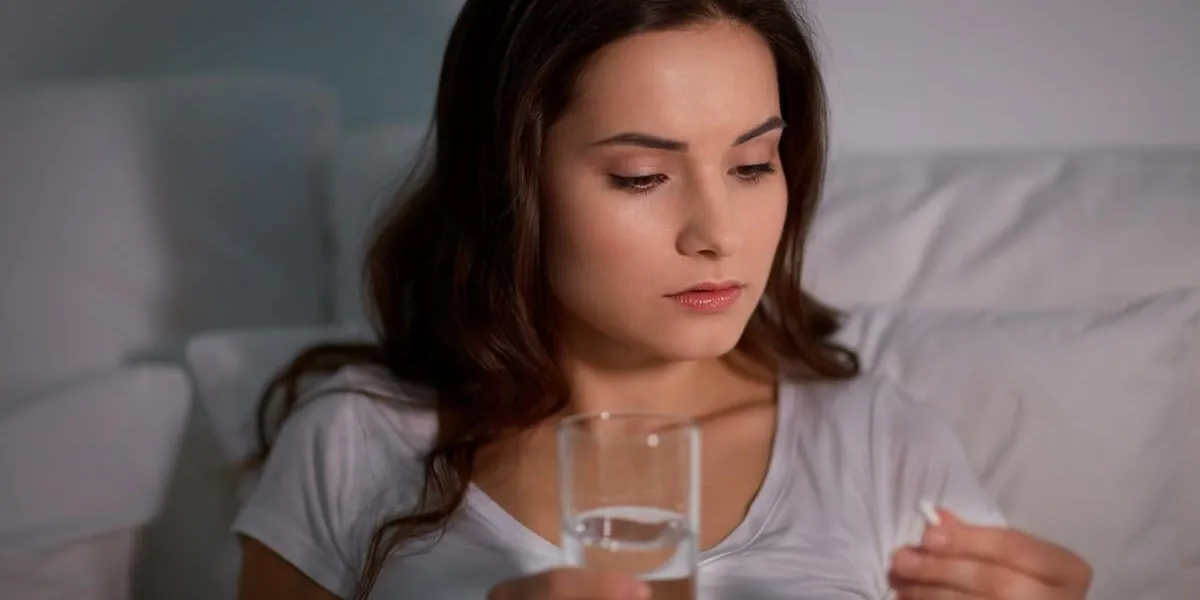 medicine, healthcare and people concept - woman with pill and glass of water in bed at night home
