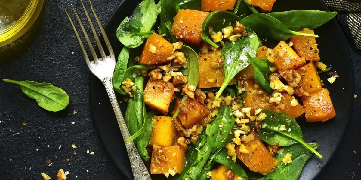 roasted pumpkin salad with spinach and walnut on a black plate on a stone backgroundtop view