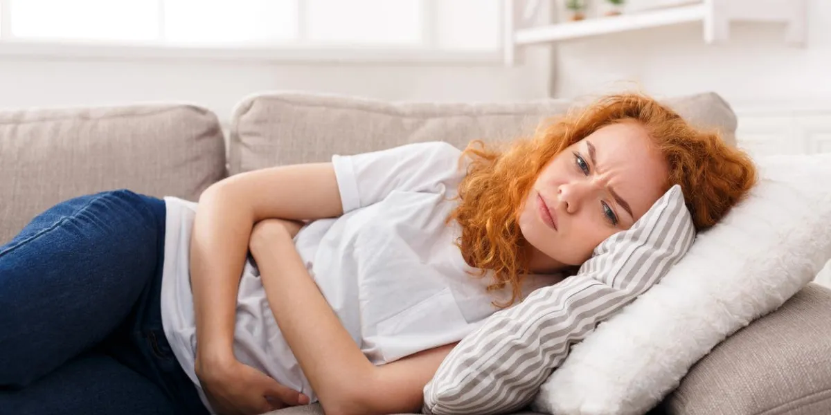 young woman suffering from stomach cramp lying on sofa at home unhealthy female with hands on her tummy