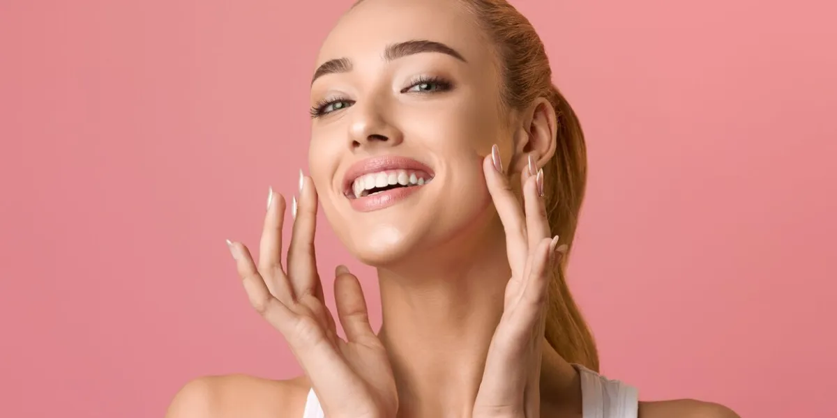 portrait of beautiful woman touching skin or applying cream over pink background