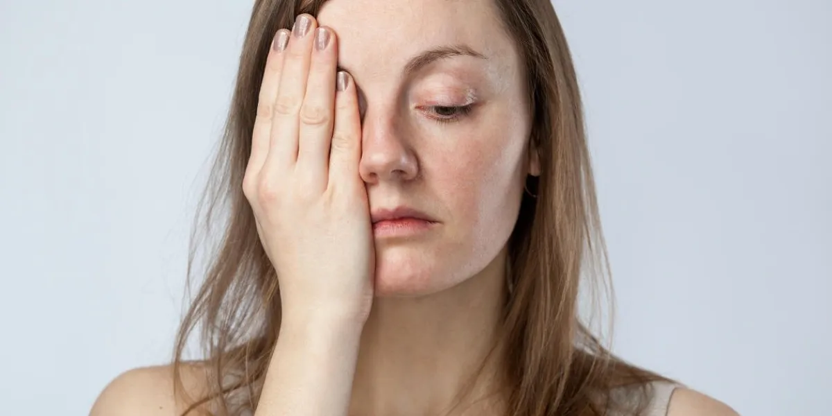 portrait d'une femme triste dans une chemise beige fermant un œil avec la main, isolé sur fond blanc froid gros plan
