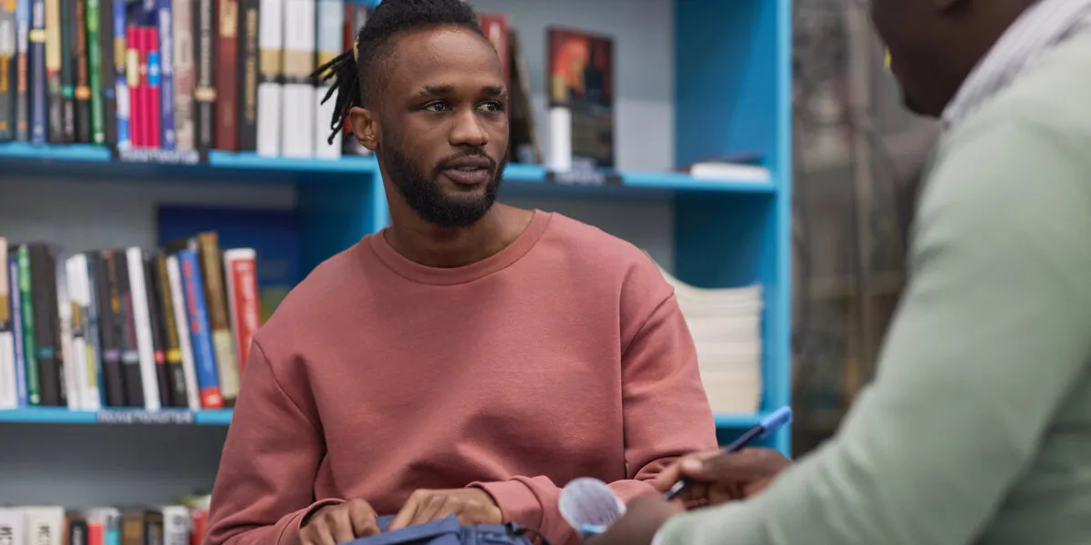 portrait of black young man talking to therapist of guidance counsellor in college library
