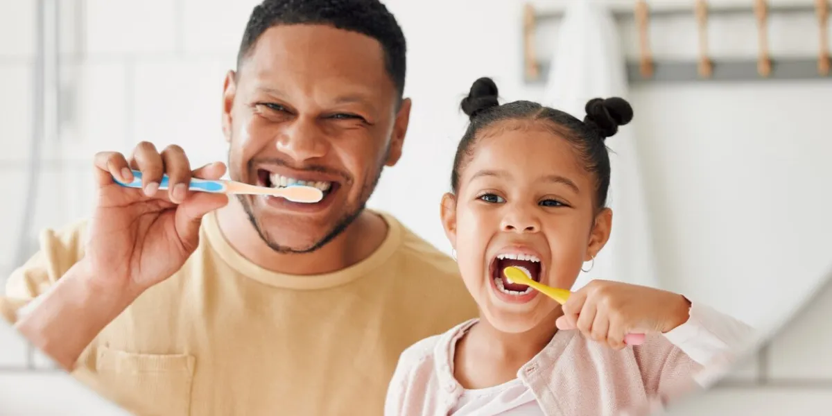 happy mixed race father and daughter brushing their teeth together in a bathroom at home single african american parent teaching his daughter to protect her teeth