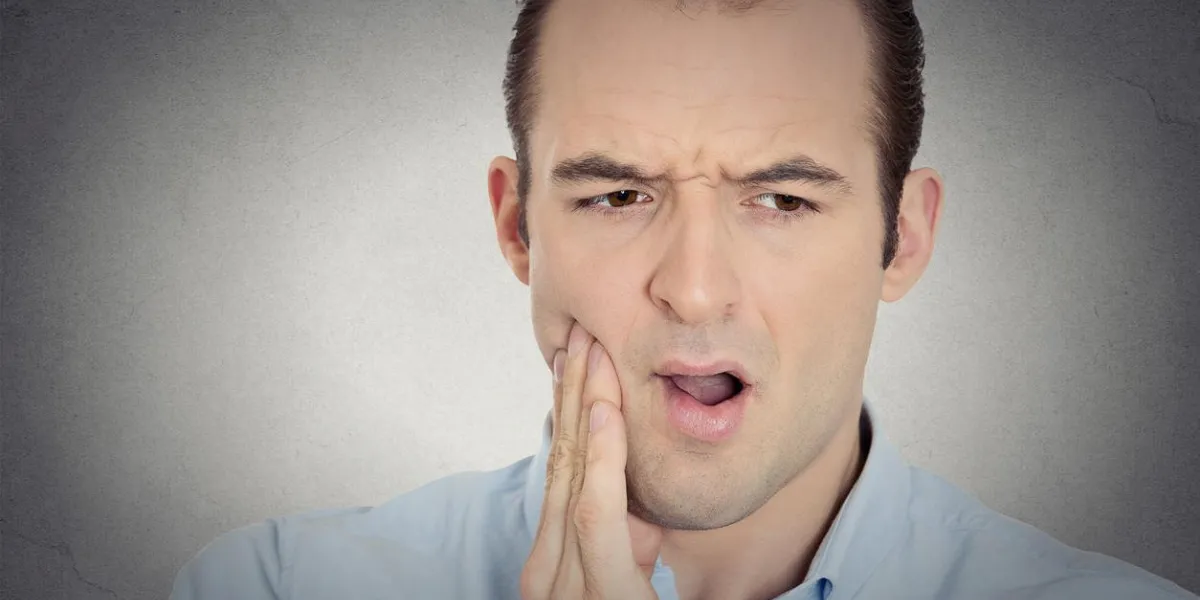 closeup portrait headshot young man with sensitive tooth ache crown problem suffering from pain touching outside mouth with hand isolated grey background negative emotions, facial expression, feeling