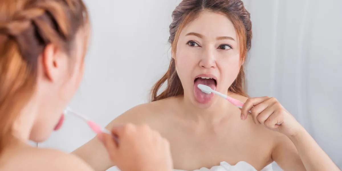 woman cleaning tongue using toothbrush with mirror in the bathroom