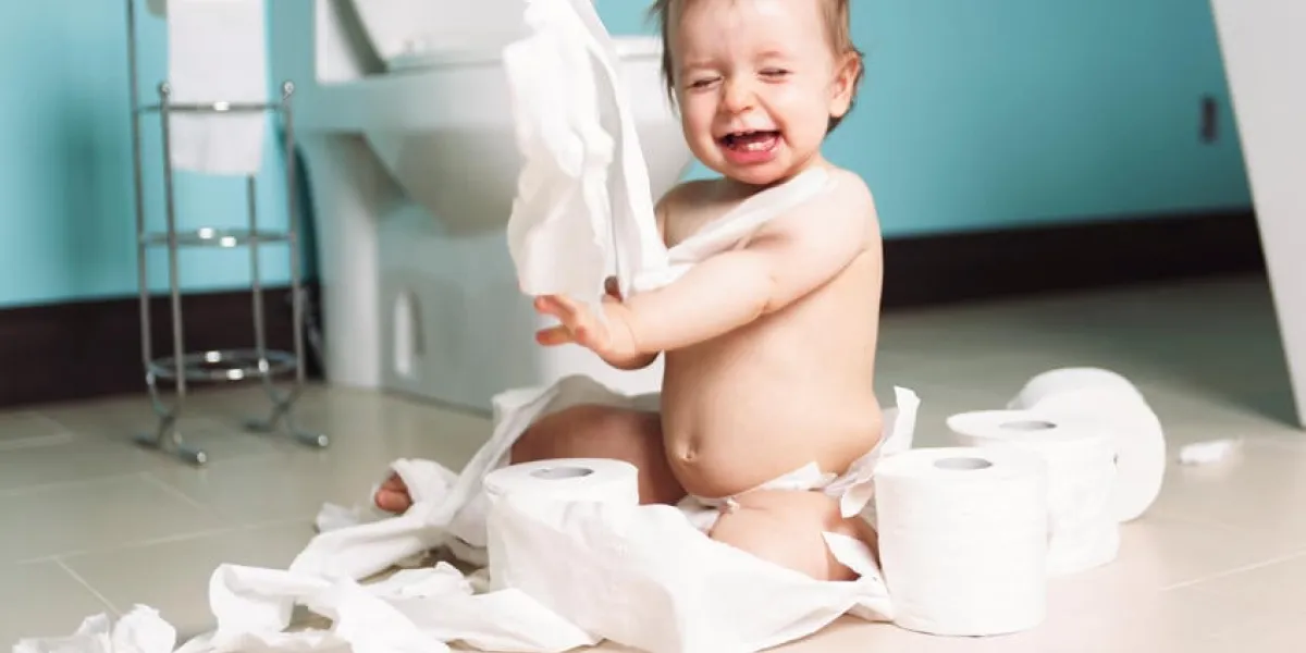 un bambin déchirant avec du papier toilette dans la salle de bain