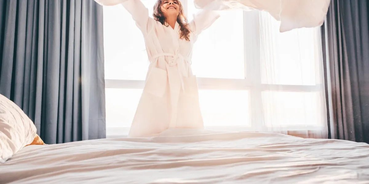 woman making bed in the sunny morning woman doing morning routine