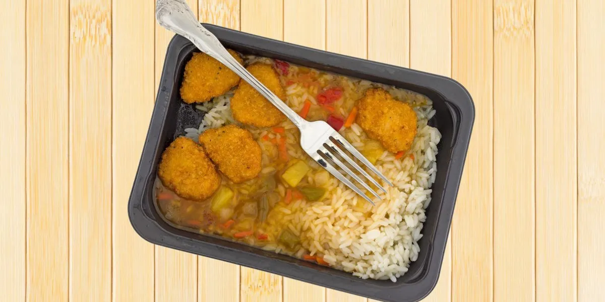 vue de dessus d'un dîner fraîchement cuit tv de poulet aigre-doux dans un plateau en plastique noir avec une fourchette dans la nourriture au sommet d'un tapis de table en bois