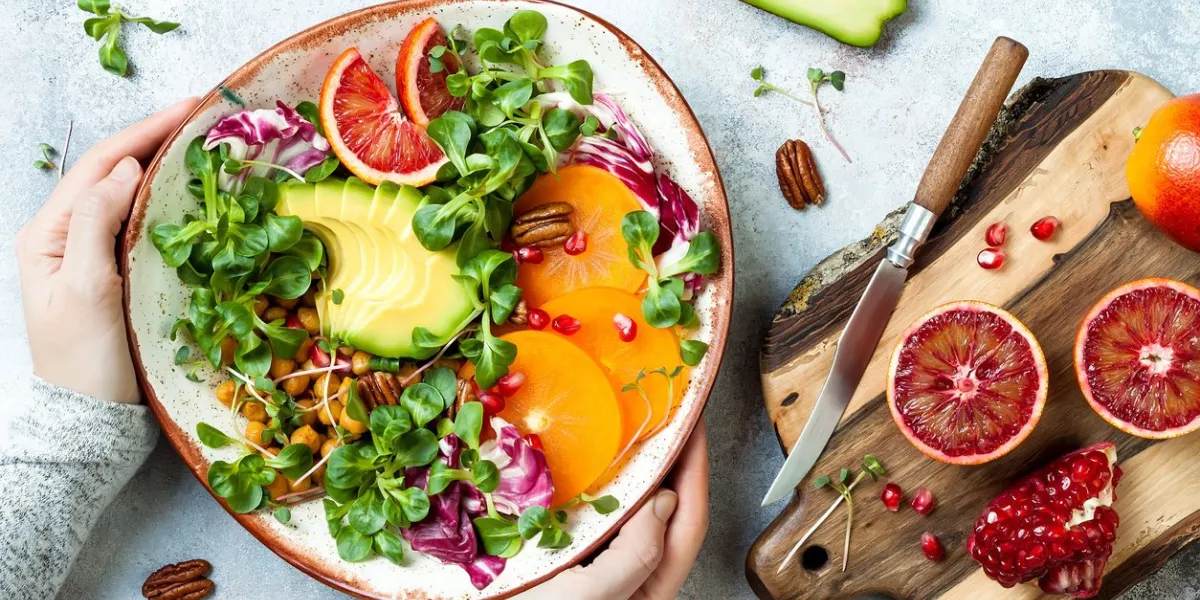 vegan, detox buddha bowl with turmeric roasted chickpeas, greens, avocado, persimmon, blood orange, nuts and pomegranate top view, flat lay