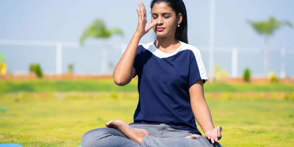 young girl doing nostril breathing exercise or pranayama yoga with closed eyes at park - concept of self care, mindfulness and active morning routine