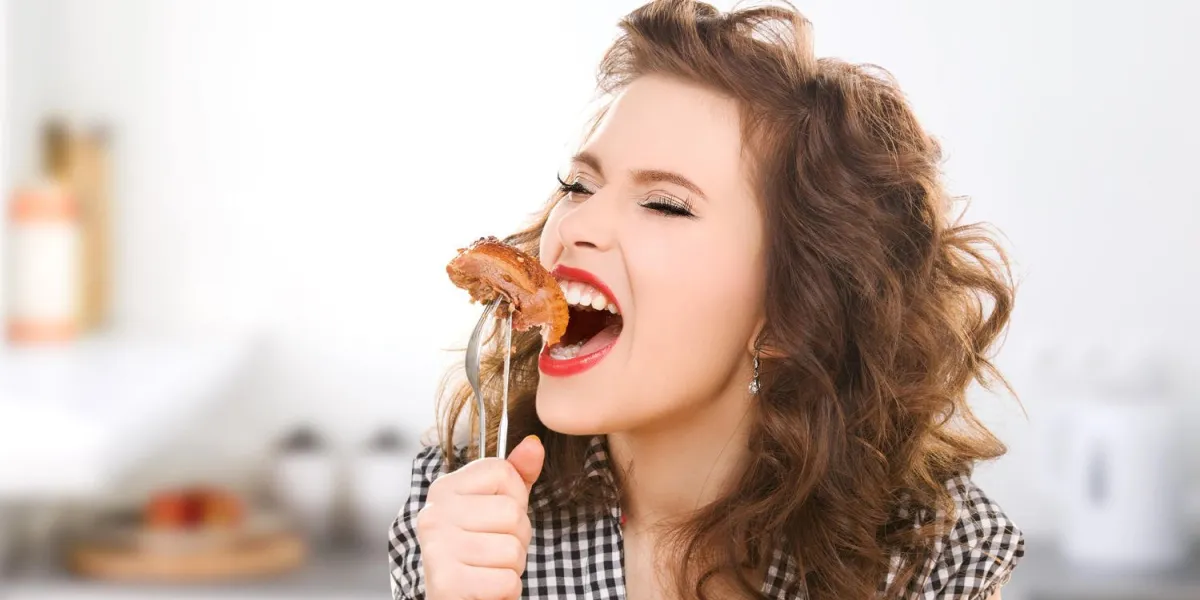 concept de personnes, alimentation, culinaire et alimentaire - faim jeune femme manger de la viande sur la fourche sur fond de cuisine