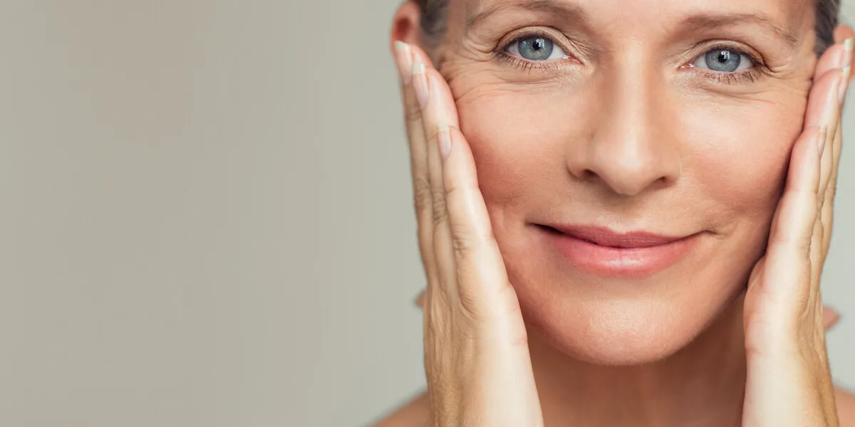 portrait of beautiful senior woman touching her perfect skin and looking at camera closeup face of mature woman with wrinkles massaging face isolated over grey background aging process concept