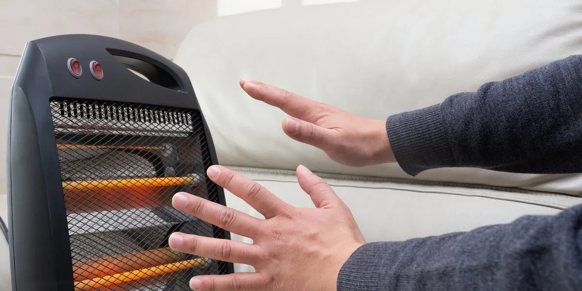 man sitting on sofa and warming up his hands with an electric heater