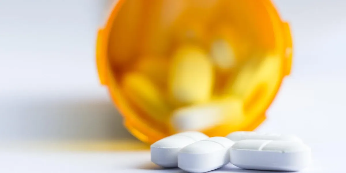 close up of a group of white tablets with an out of focus prescription bottle in the background